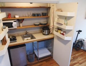 A tiny kitchen with a single stovetop, small sink and refrigerator is nestled behind dual doors. Banner Photo