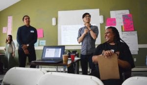 Lucas Turner-Owens, fund manager; Aaron Tanaka, co-founder of Boston Ujima Project; and Nia Evans, executive director of Boston Ujima Project lead a participatory voting process during the June 9 assembly. Banner Photo
