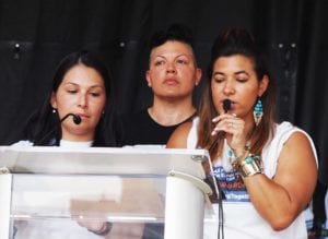 Natalie Sanchez, president of March Forward Massachusetts, speaks on the Boston Common as actor Sara Ramirez (center) and Melissa Luna (right) share the podium. Banner Photo