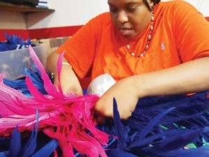 Kwesi Matthew attaches feathers to a headpiece. Banner Photo