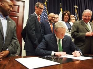 Gov. Charlie Baker signs into law criminal justice reforms that eliminated mandatory minimum sentences for nonviolent drug offenses as legislative leaders look on. — Banner Photo