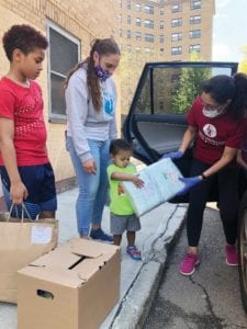 USES volunteer Silvia Buonamici hands over a package of diapers to 2-year-old Logan with his mother, Gabriela Cruzado, and his brother, Troy, Standing curbside. PHOTO: ERINT IMAGES